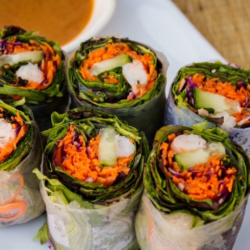 Six fresh spring rolls filled with shrimp, shredded carrots, cucumber, and lettuce, with peanut sauce.