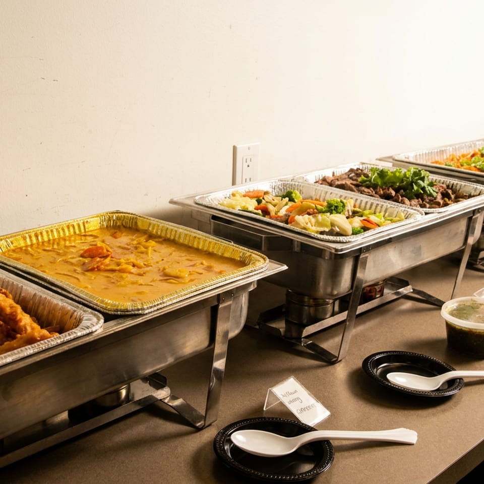 A buffet line with several chafing dishes filled with various hot foods, including fried chicken and curry.